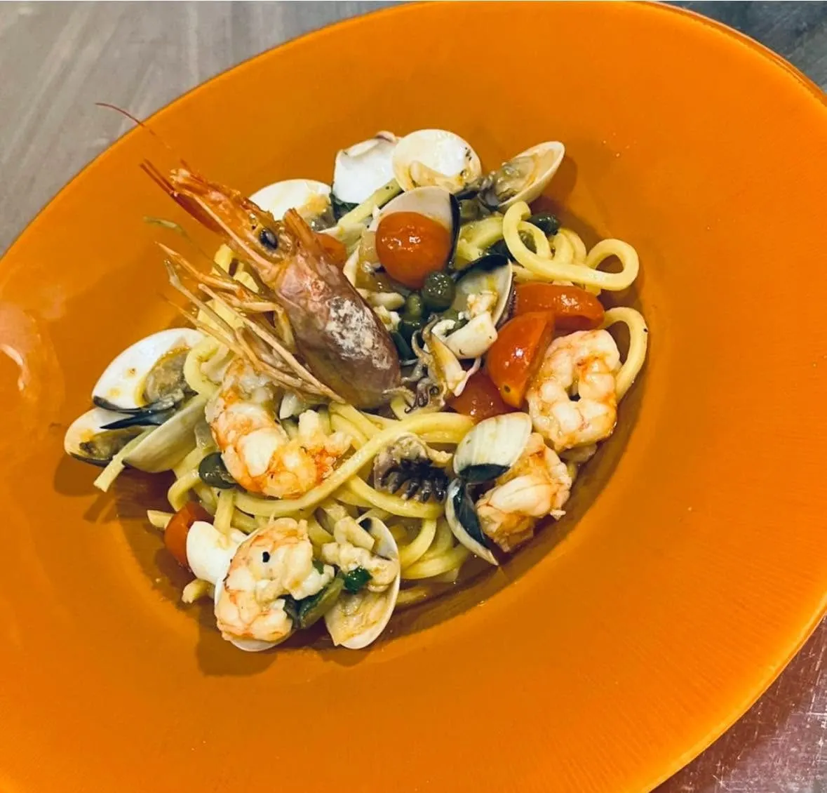 Pasta fresca con gambas, almejas y tomate cherry en un plato naranja