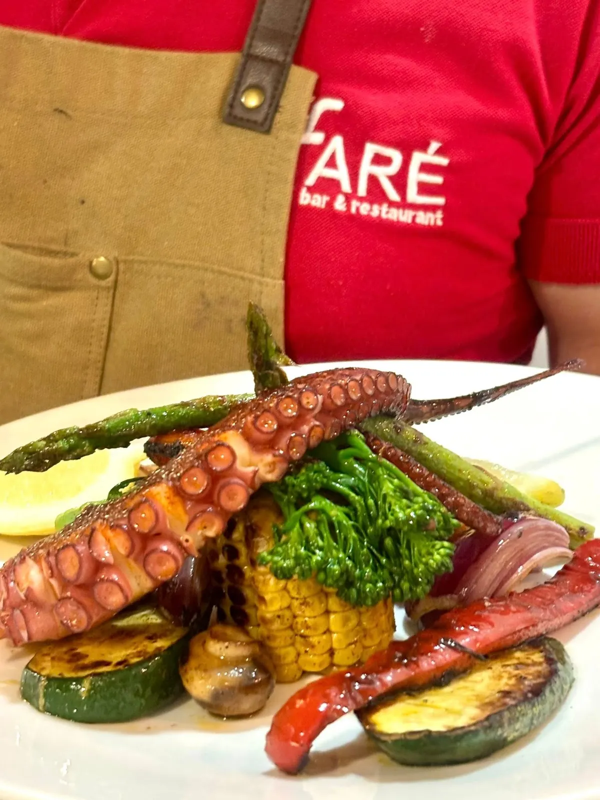 Pulpo a la plancha con verduras a la brasa, servido en plato blanco