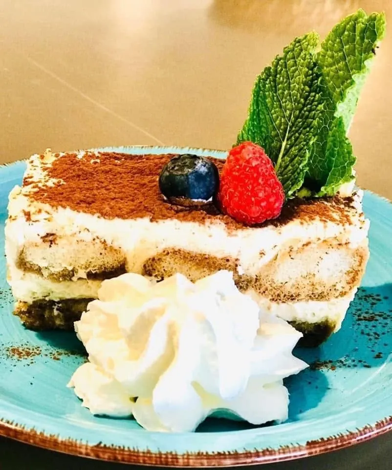 Porción de tiramisú casero con nata, frambuesa, arándano y hojas de menta